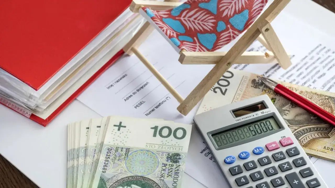 Kalkulator, pieniądze i miniaturowa leżanka sugerują planowanie wakacji i świadczenie urlopowe.
