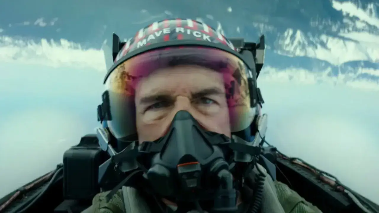Tom Cruise jako Maverick w hełmie z napisem "MAVERICK" w filmie Top Gun: Maverick. Intensywne spojrzenie pilota w kokpicie myśliwca.