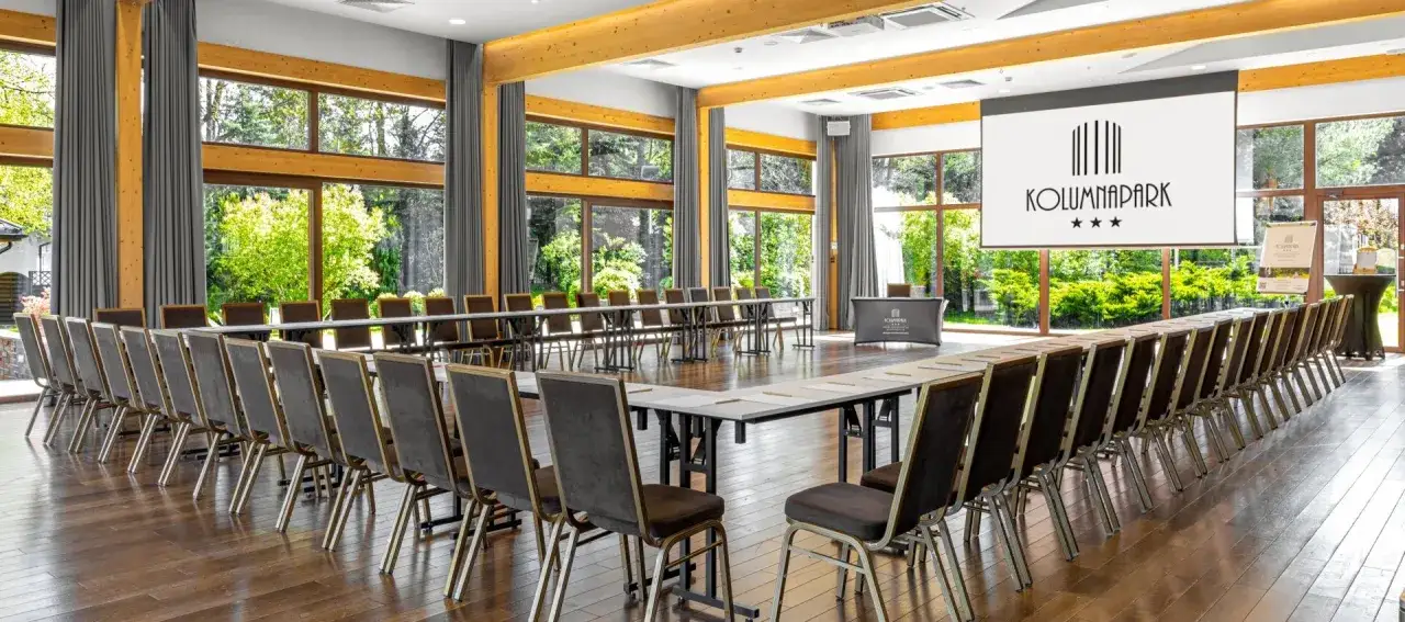 Sala konferencyjna w hotelu Kolumna Park z widokiem na zieleń. Ustawienie stołów w kształt podkowy, gotowa na spotkanie.