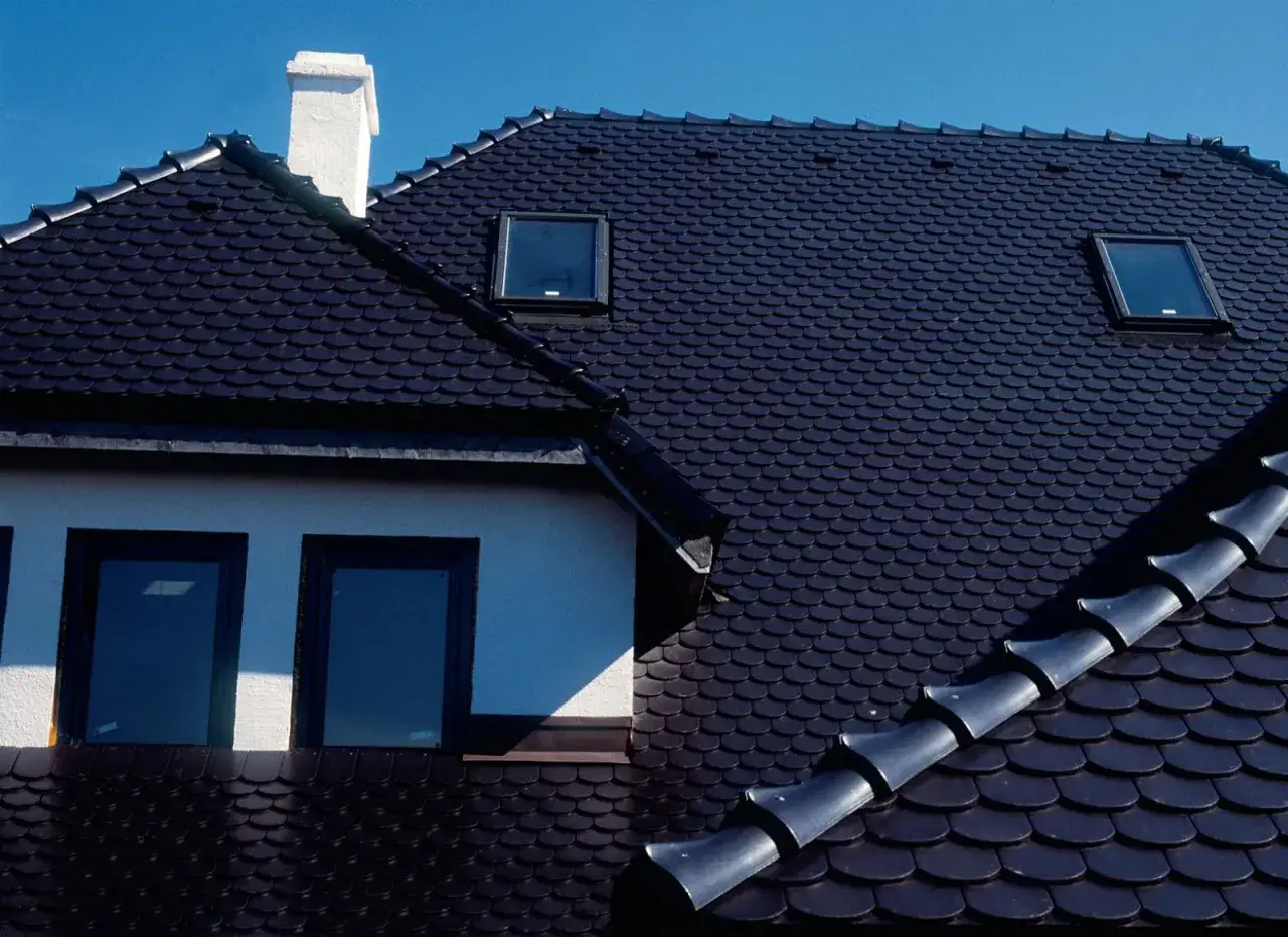 Ciemny dach z dachówki ceramicznej, z kominem i oknami dachowymi. Zastanawiasz się, ile waży paleta dachówki ceramicznej?