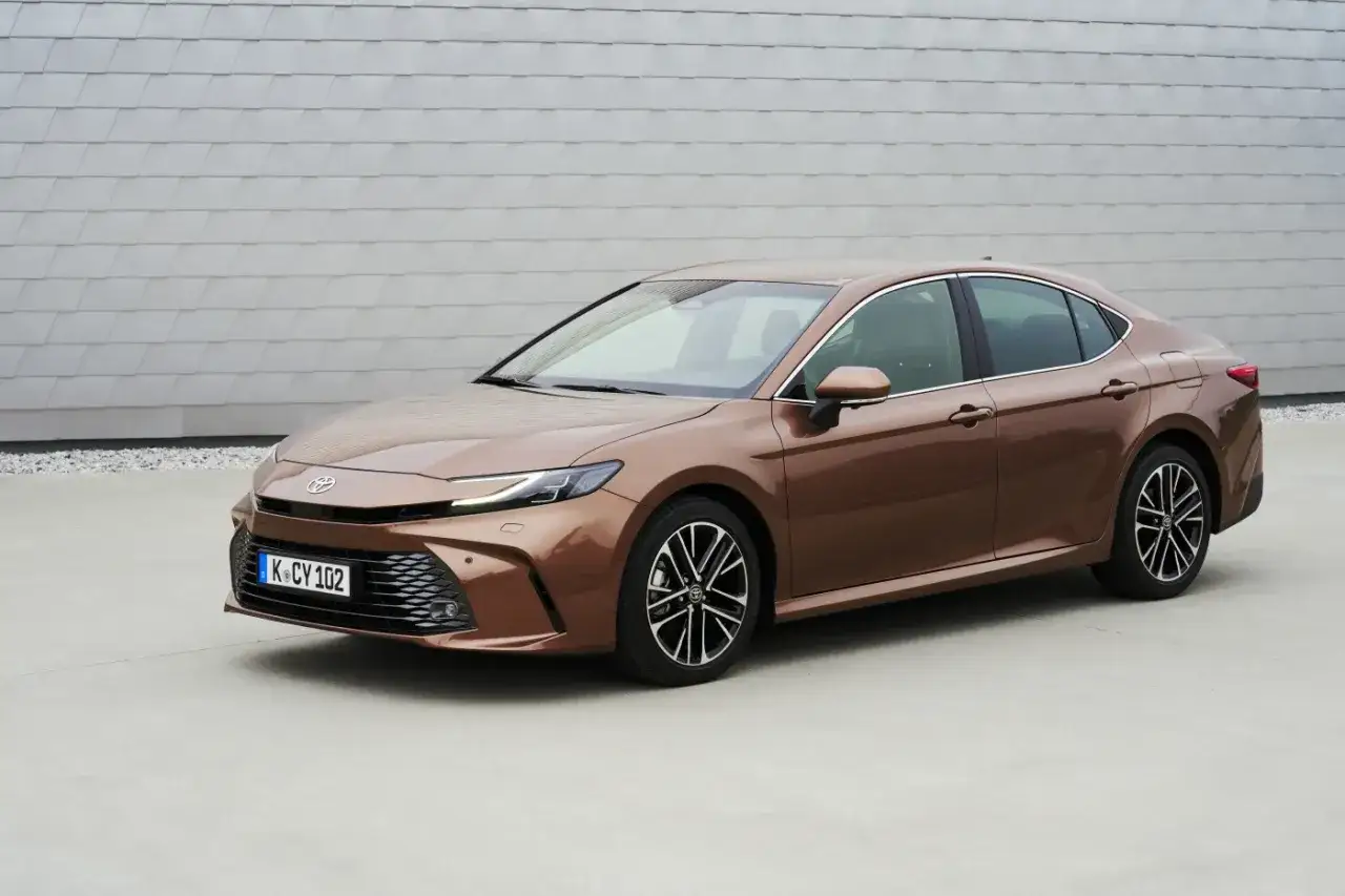 Elegancka, nowa Toyota Camry w kolorze brązowym prezentuje się stylowo na tle nowoczesnej architektury.