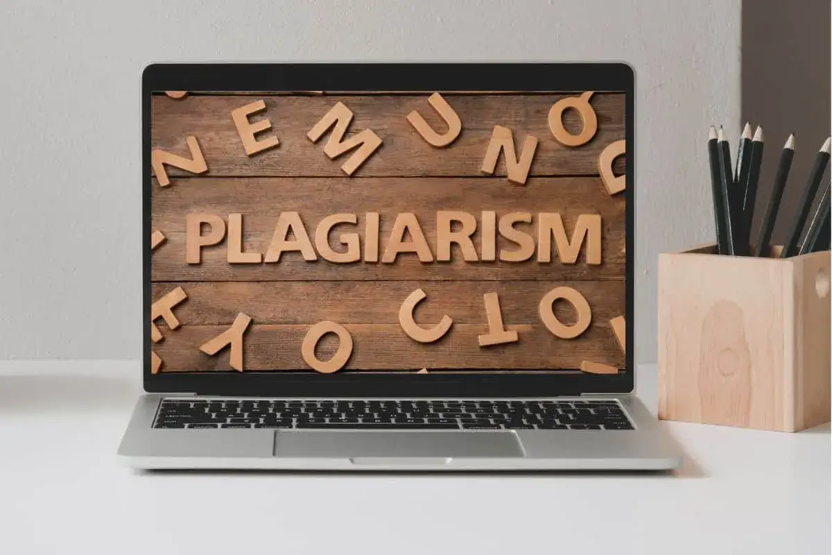 Laptop z napisem "PLAGIARISM" ułożonym z drewnianych liter na tle desek.