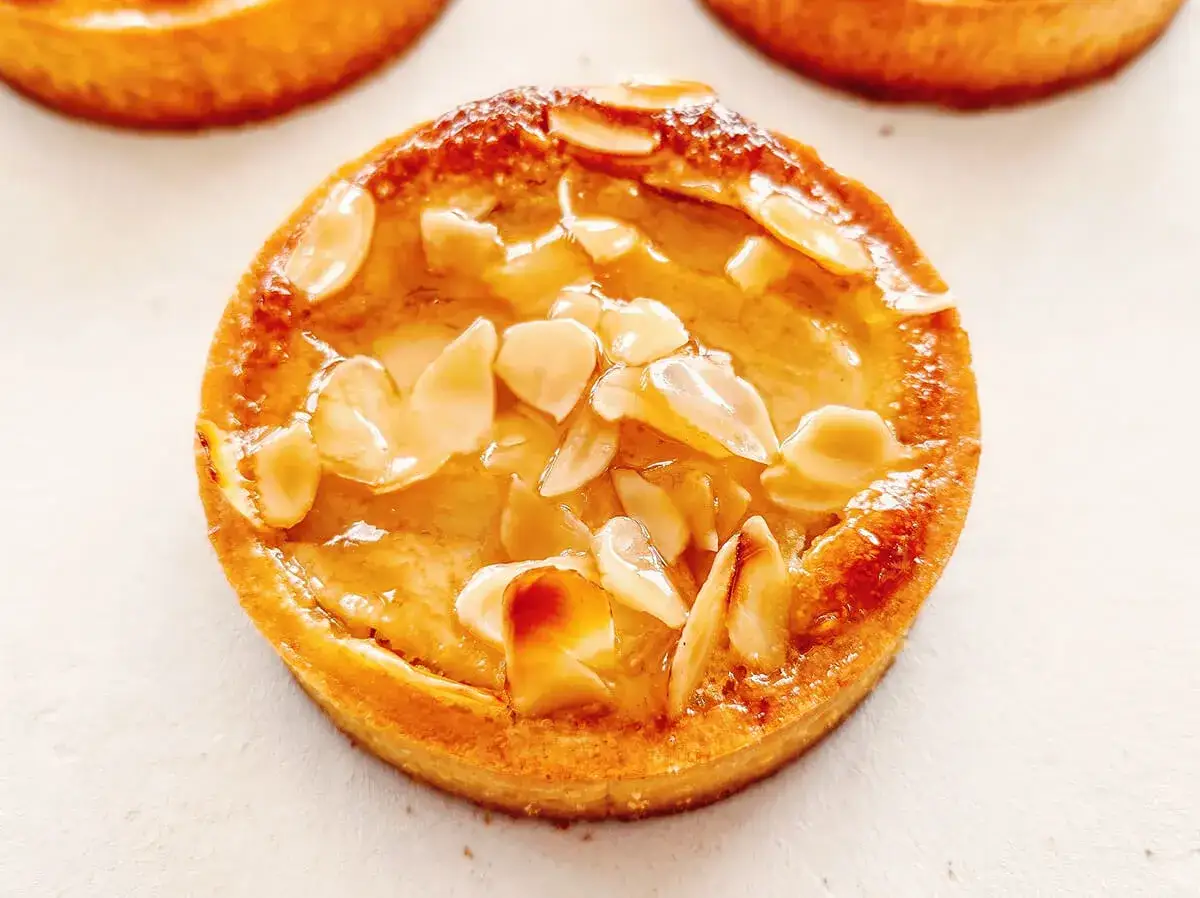 Un délicieux gâteau poire amandine, doré et garni d'amandes effilées, prêt à être dégusté.