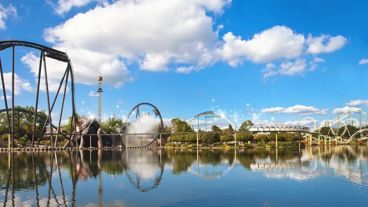 Aussicht auf Achterbahnen und einen Freizeitpark mit Spiegelung im Wasser.