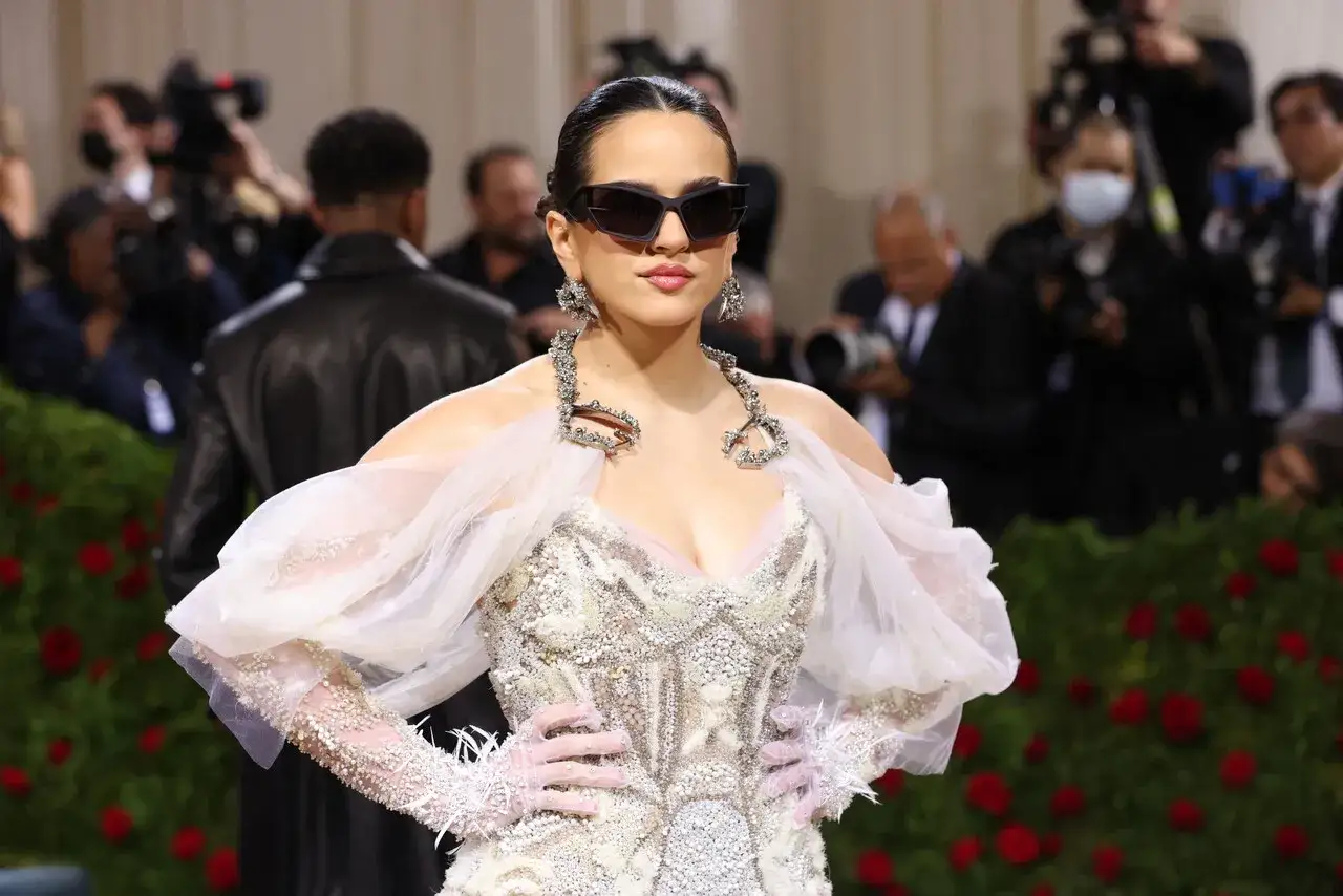 Rosalía deslumbrante en la Met Gala, con un vestido blanco adornado y gafas de sol vanguardistas.