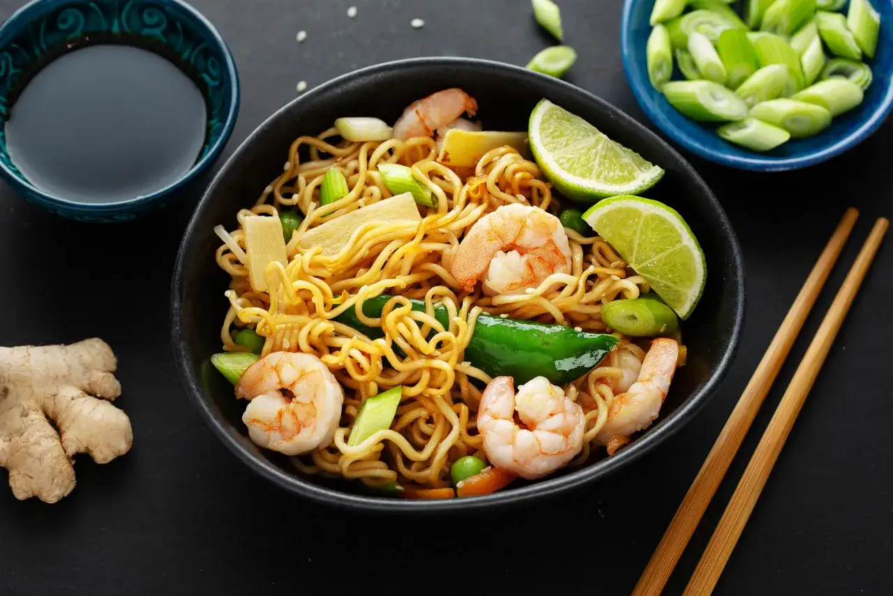 Makaron chow mein z krewetkami, warzywami i limonką, podany z sosem sojowym i imbirem.