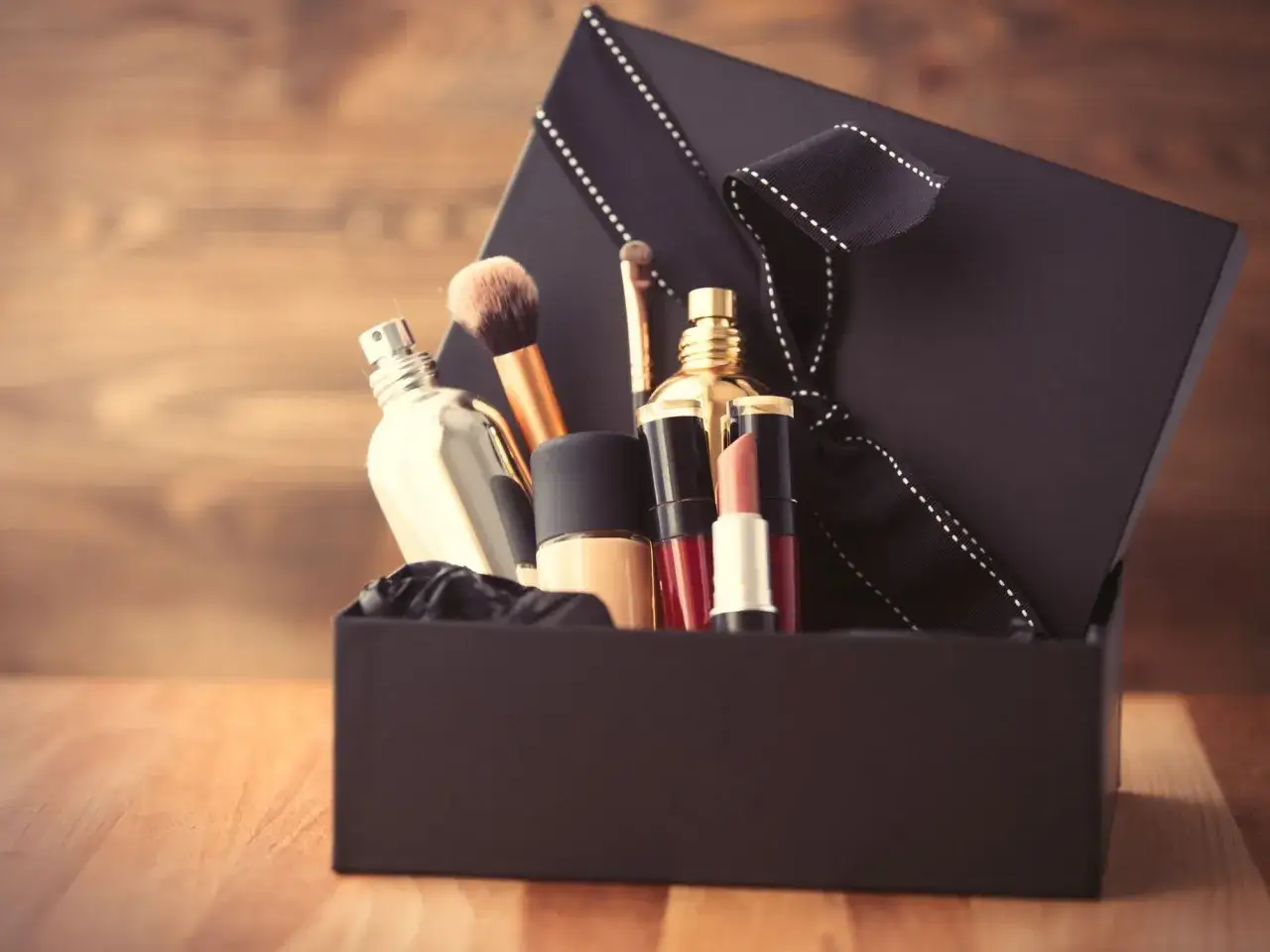 Schwarze Geschenkbox mit Kosmetikartikeln wie Parfüm, Lippenstift und Make-up-Pinseln.