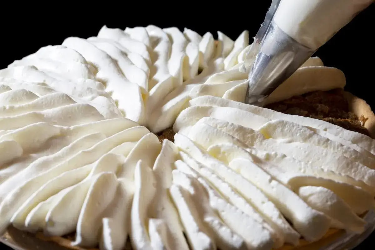 Garniture d'une tarte avec une poche à douille, évoquant la recette crémeux vanille Michalak.
