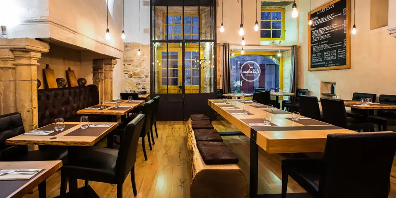 Ambiance chaleureuse au restaurant "Les Fougeres". Tables en bois brut, banquette en cuir et cheminée imposante créent un décor rustique et élégant.