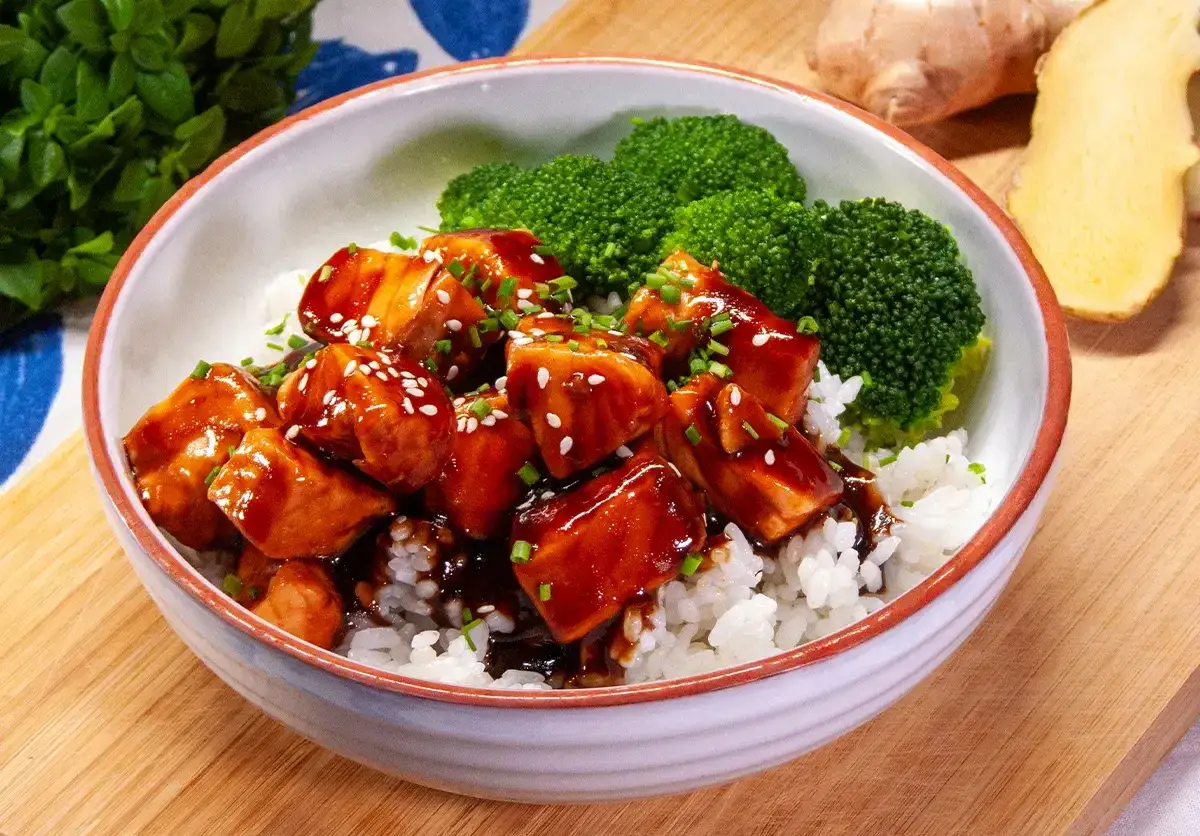 Aksamitny łosoś w sosie teriyaki, podany z ryżem i brokułami, posypany sezamem i szczypiorkiem. Pyszne danie gotowe do spożycia.