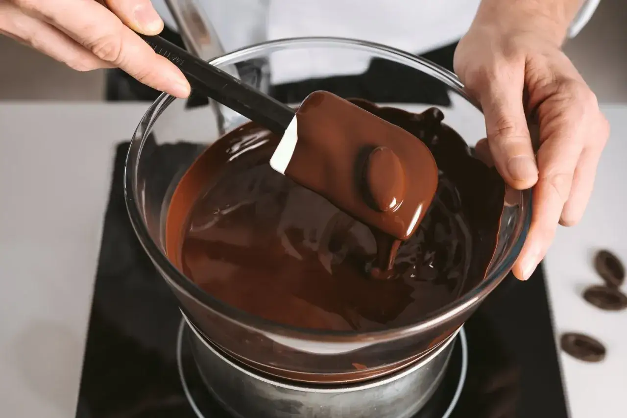 Un chocolat qui ne fond pas ? Ce n'est pas le cas ici ! Une spatule mélange du chocolat fondu brillant dans un bol en verre au-dessus d'un bain-marie.