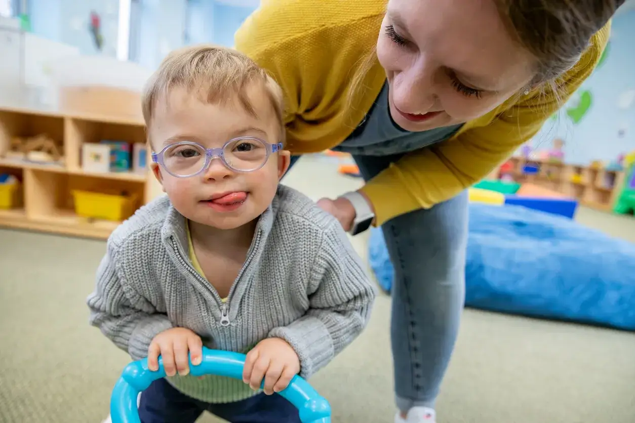 Chłopiec z zespołem Downa, w okularach, z językiem na brodzie, bawi się z terapeutką. To przykład pracy w obszarze oligofrenopedagogiki.