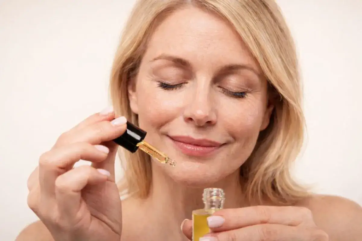 Kobieta z zamkniętymi oczami aplikuje serum z **retinolem**, dbając o skórę, by uniknąć efektów **solarium**.