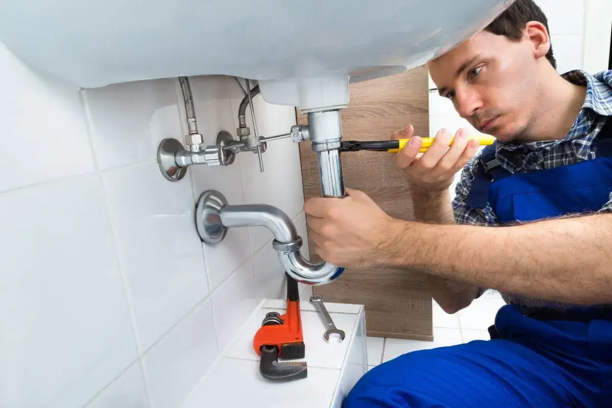 Monter instalacji sanitarnych dokręca kluczem syfon pod umywalką.