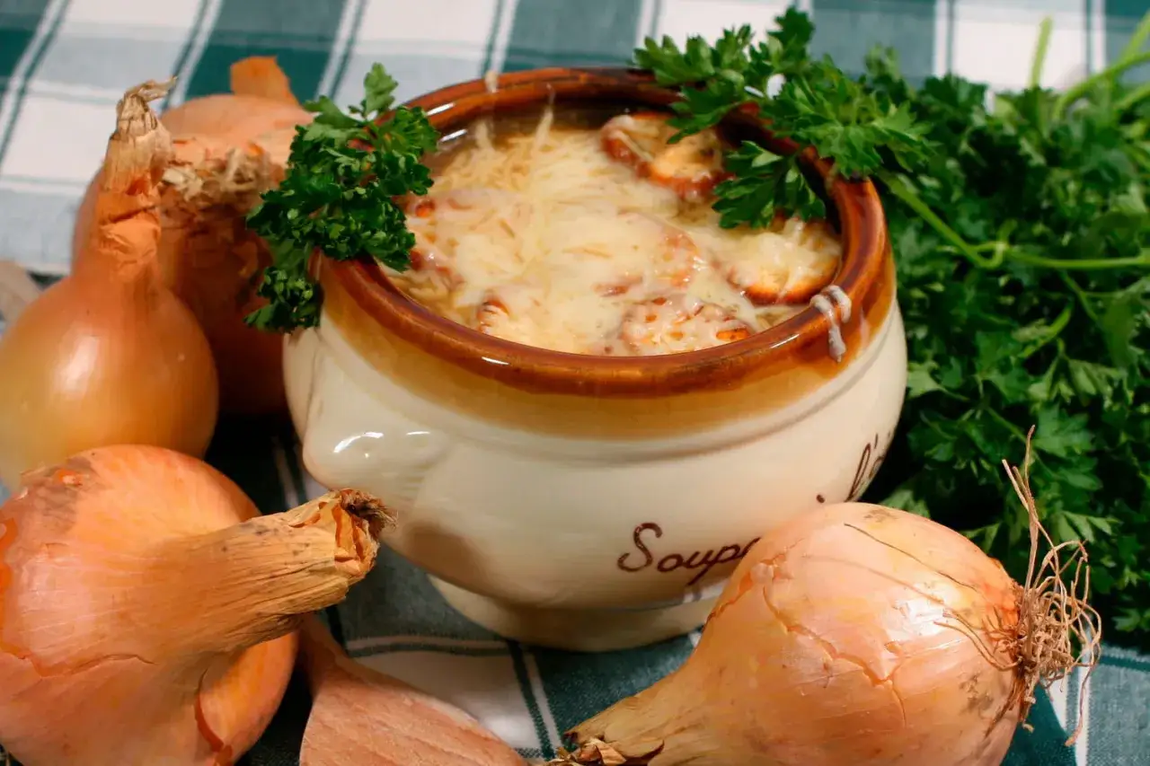 Un bol de soupe à l'oignon gratinée, un plat parisien réconfortant, entouré d'oignons frais et de persil.