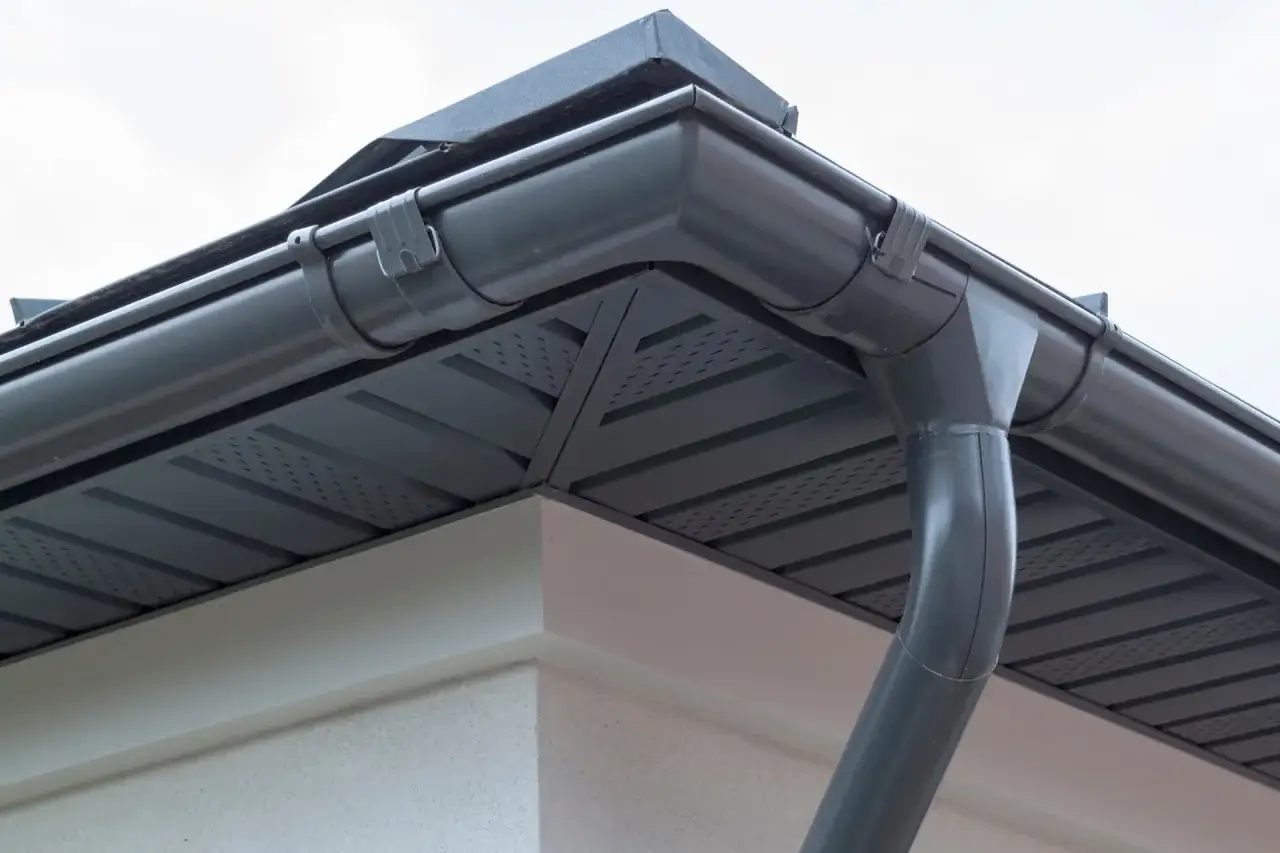 Szary system rynnowy z rurą elastyczną do rynny, zamontowany na rogu dachu.