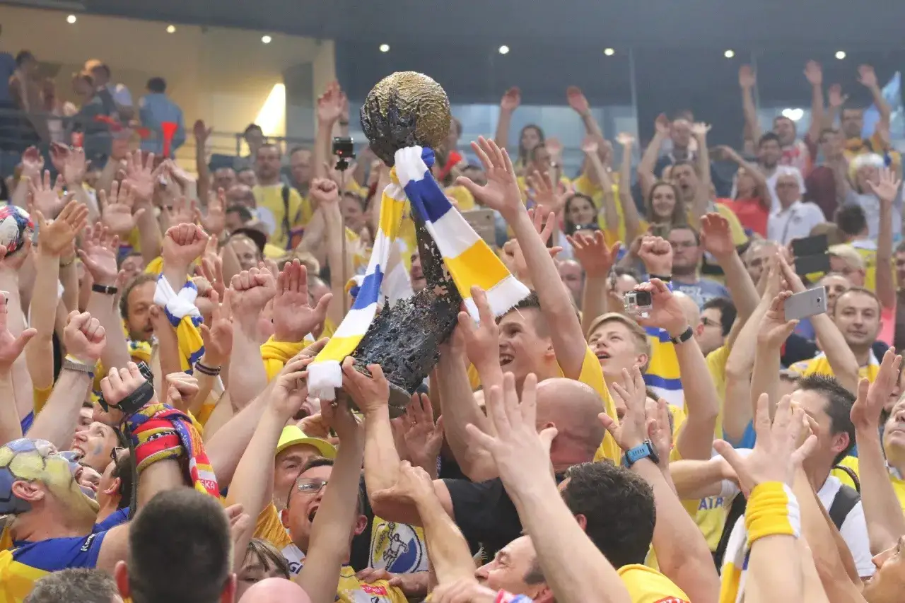 Tłum świętuje zwycięstwo, unosząc puchar. Kibice w żółto-niebieskich barwach, jak na meczach kielce liga mistrzów, cieszą się z sukcesu.