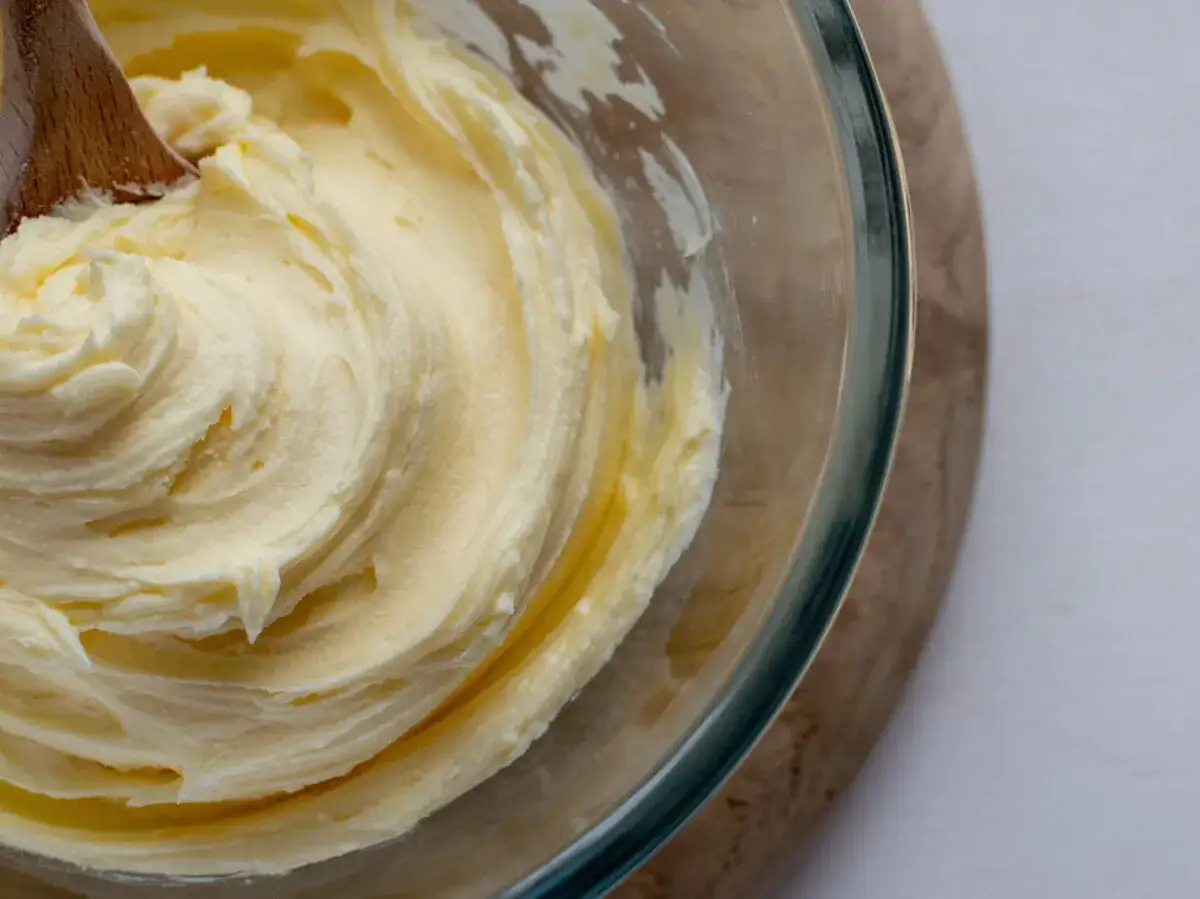 Une cuillère en bois mélange une crème au beurre traditionnelle onctueuse dans un bol en verre.