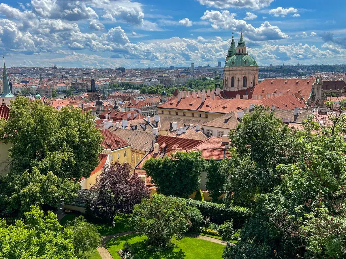 Widok na dachy Pragi z zielonym ogrodem. W oddali widać kopułę kościoła. Idealne miejsce, by zobaczyć w Pradze piękno architektury.