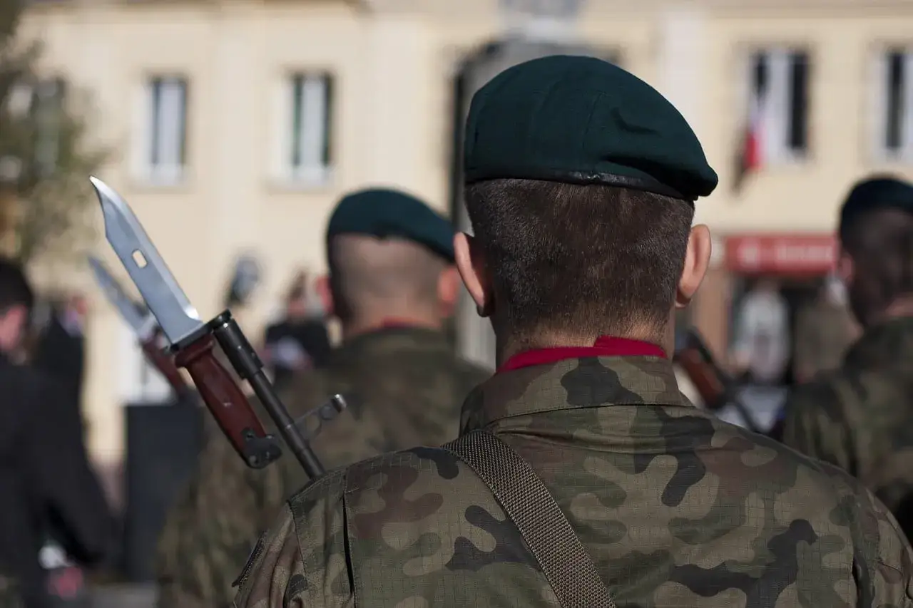 Żołnierze w mundurach moro i zielonych beretach, z bagnetami na karabinach.