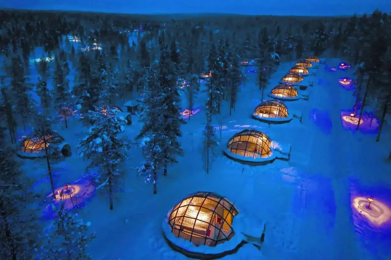 Szklane igloo w zaśnieżonym lesie, gdzie jest Laponia. Nocą rozświetlają je ciepłe światła, tworząc magiczny widok.