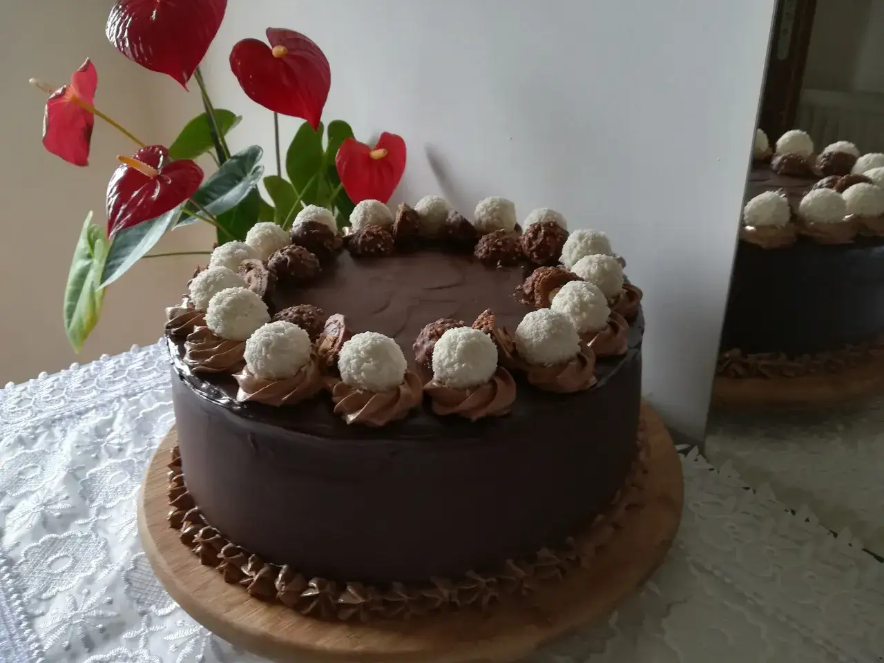 Czekoladowy tort udekorowany pralinami Lindt i Ferrero Rocher, obok czerwone anturium.