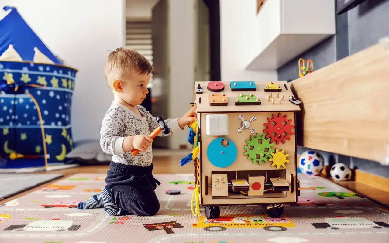 Chłopiec bawi się drewnianą kostką edukacyjną z młotkiem.