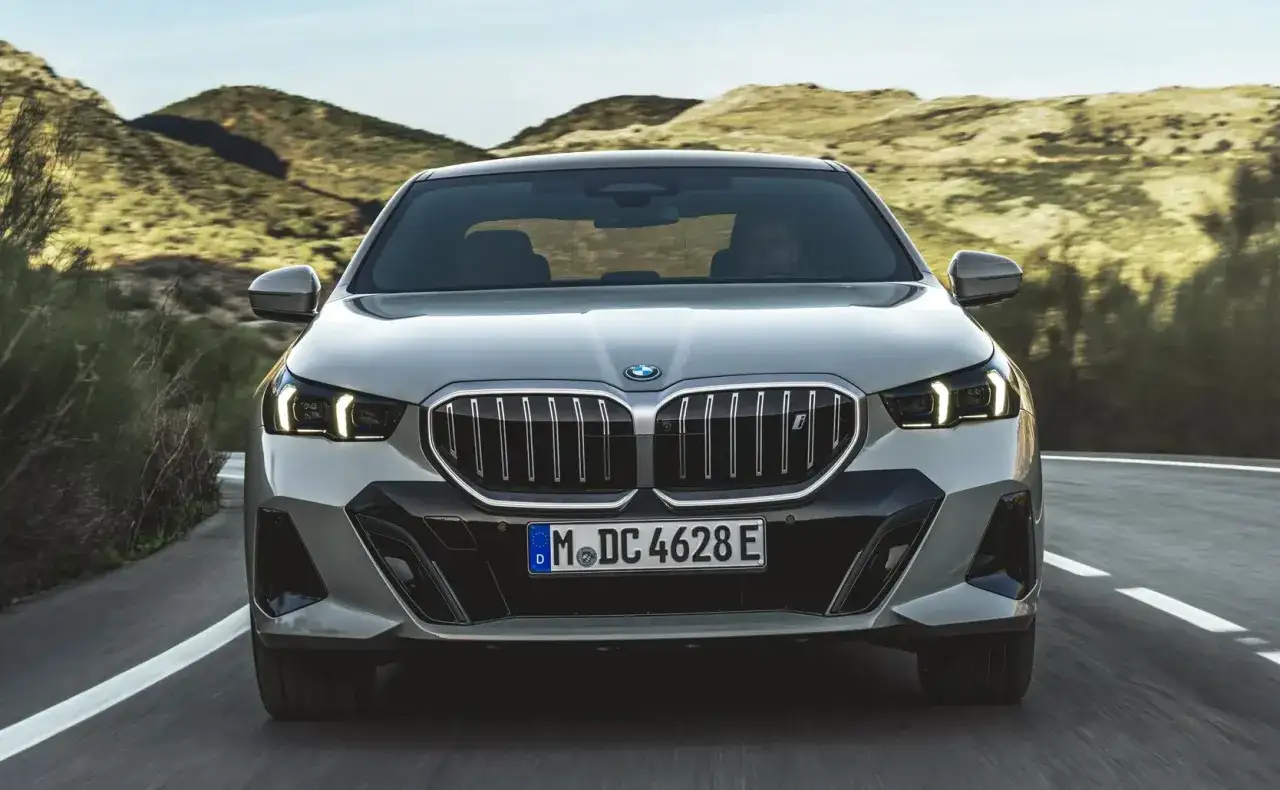 Nowe BMW 5 na krętej drodze wśród wzgórz. Elegancka sylwetka i charakterystyczny grill.