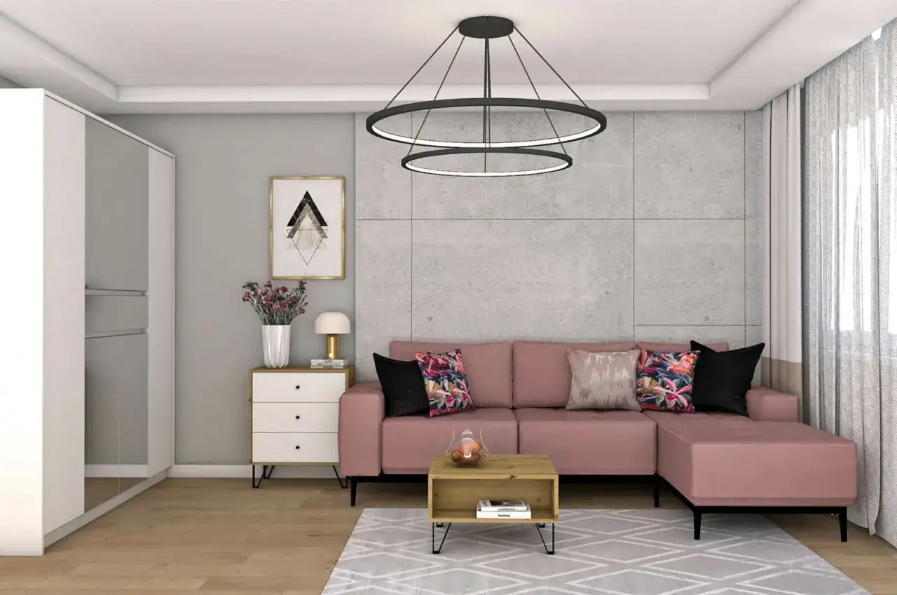 Różowa kanapa i kolorowe poduszki ocieplają szary salon. Wazon z kwiatami i stylowa lampka dodają przytulności.