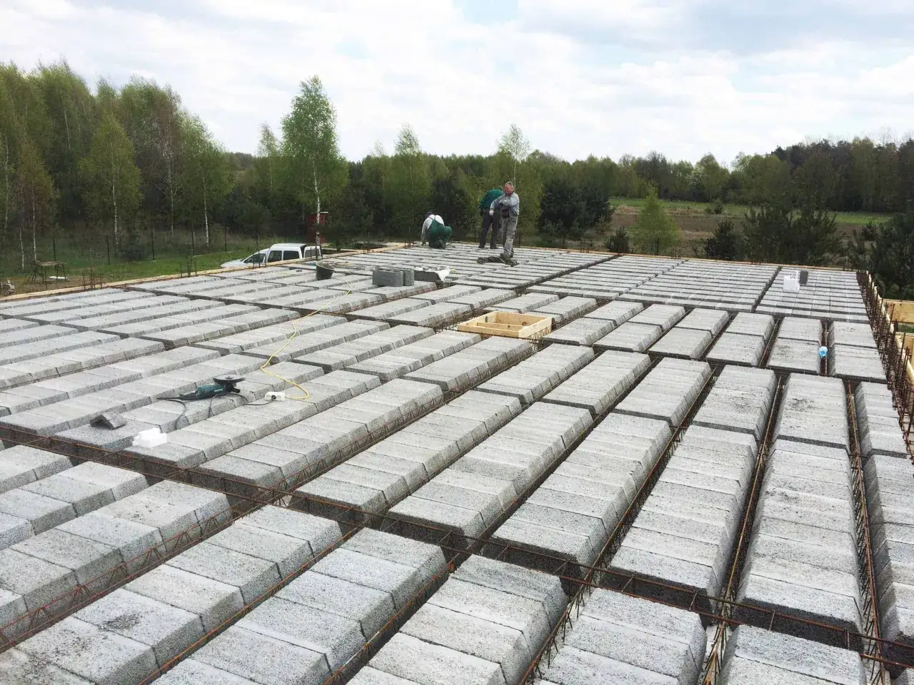 Budowa stropu gęstożebrowego z pustaków betonowych. Pracownicy układają elementy konstrukcyjne, przygotowując budynek do dalszych prac.