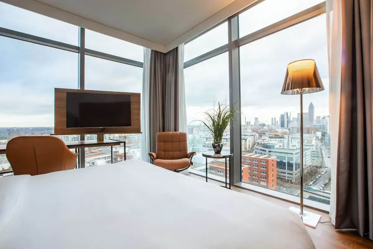 Modern Hotelzimmer mit Skyline-Blick, Bett, Sessel und Fernseher.