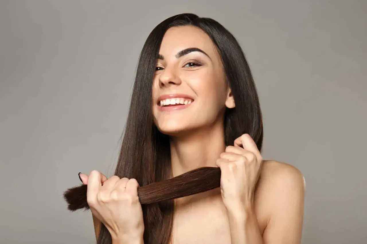 Mujer sonriente muestra su cabello largo y sedoso, un ejemplo de cómo cuidar el pelo para que luzca saludable y brillante.