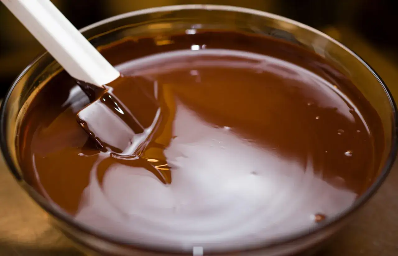 Spatule blanche remuant du chocolat fondu dans un bol en verre. Le chocolat est lisse et brillant, prêt à être utilisé pour une recette.