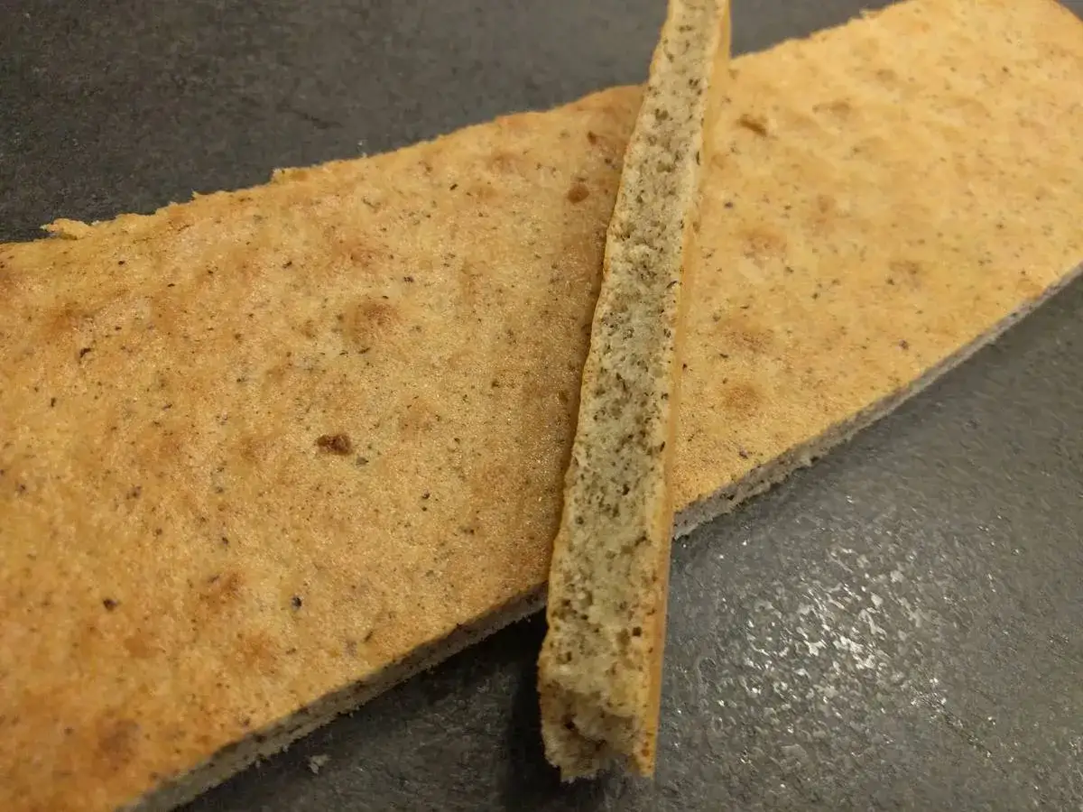 Un biscuit joconde noisette, fin et doré, est coupé en deux. Une fine tranche repose sur une plus grande pièce.