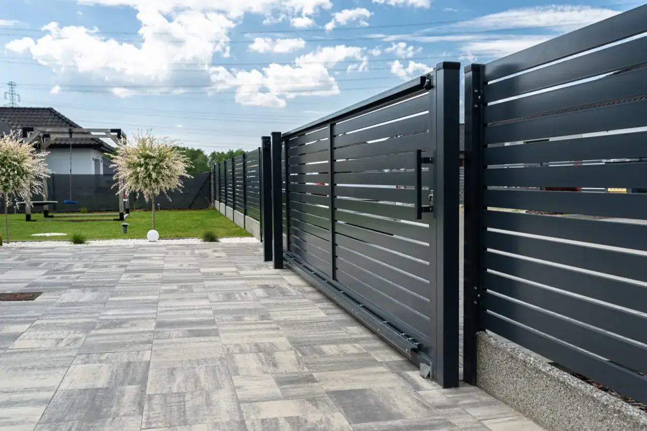 Solidny fundament pod bramę przesuwną zapewnia jej stabilność i płynne działanie. Nowoczesna, ciemnoszara brama z poziomymi lamelami.