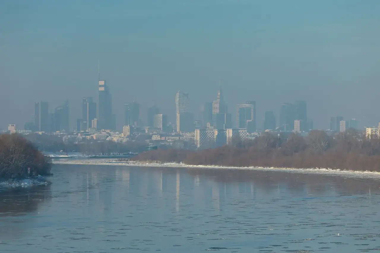 Widok na zamglone miasto z rzeką i lodem na pierwszym planie.