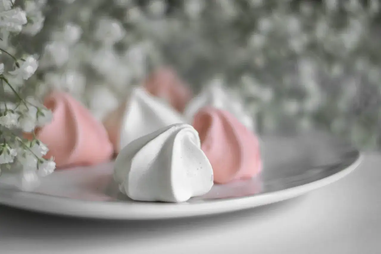 Douceur aérienne de meringue italienne rose et blanche sur une assiette, avec des petites fleurs en arrière-plan.