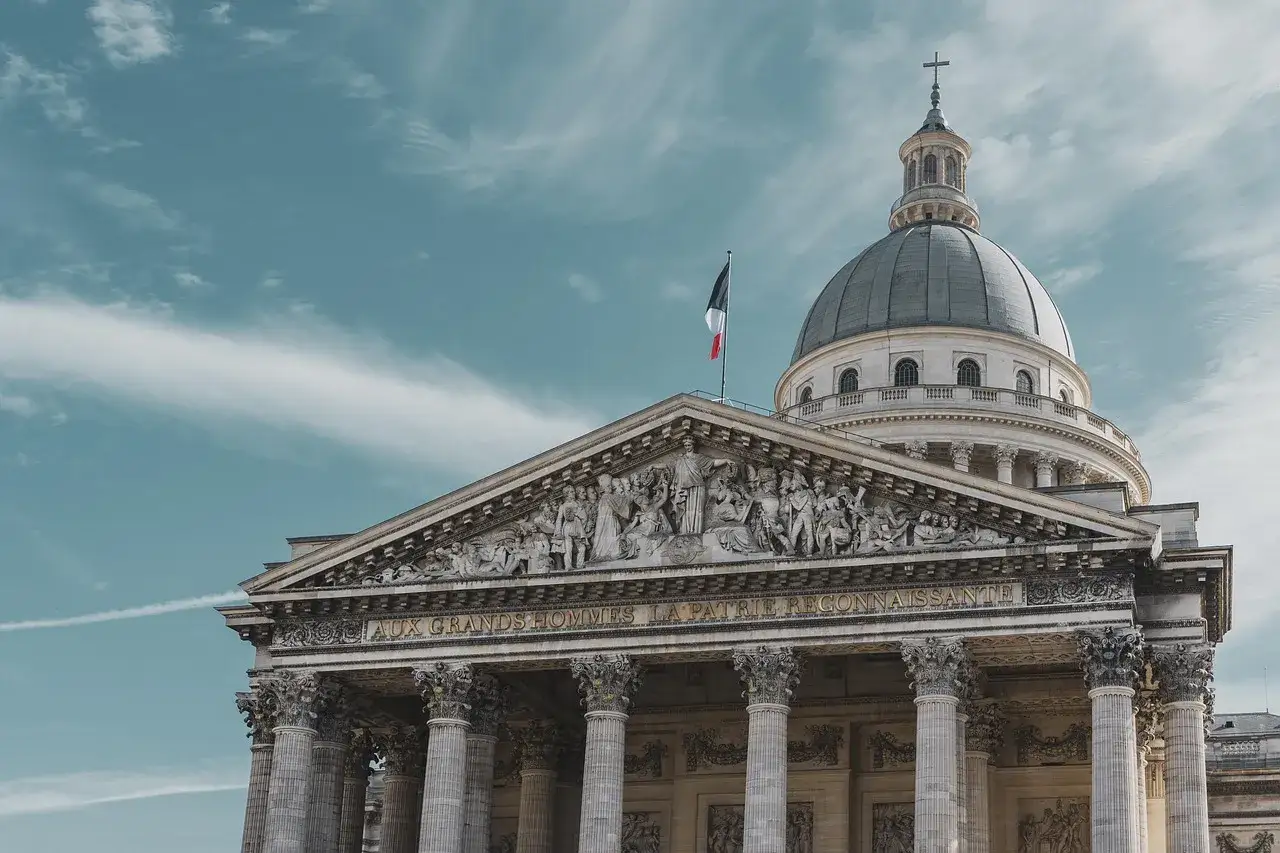 Majestatyczny Panteon w Paryżu z kopułą i francuską flagą na tle błękitnego nieba.