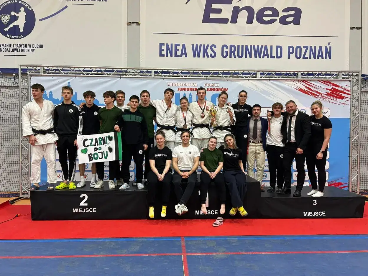 Młodzi sportowcy świętują sukces na mistrzostwa polski juniorów. Drużyna z transparentem "Czarni do boju" pozuje na podium.