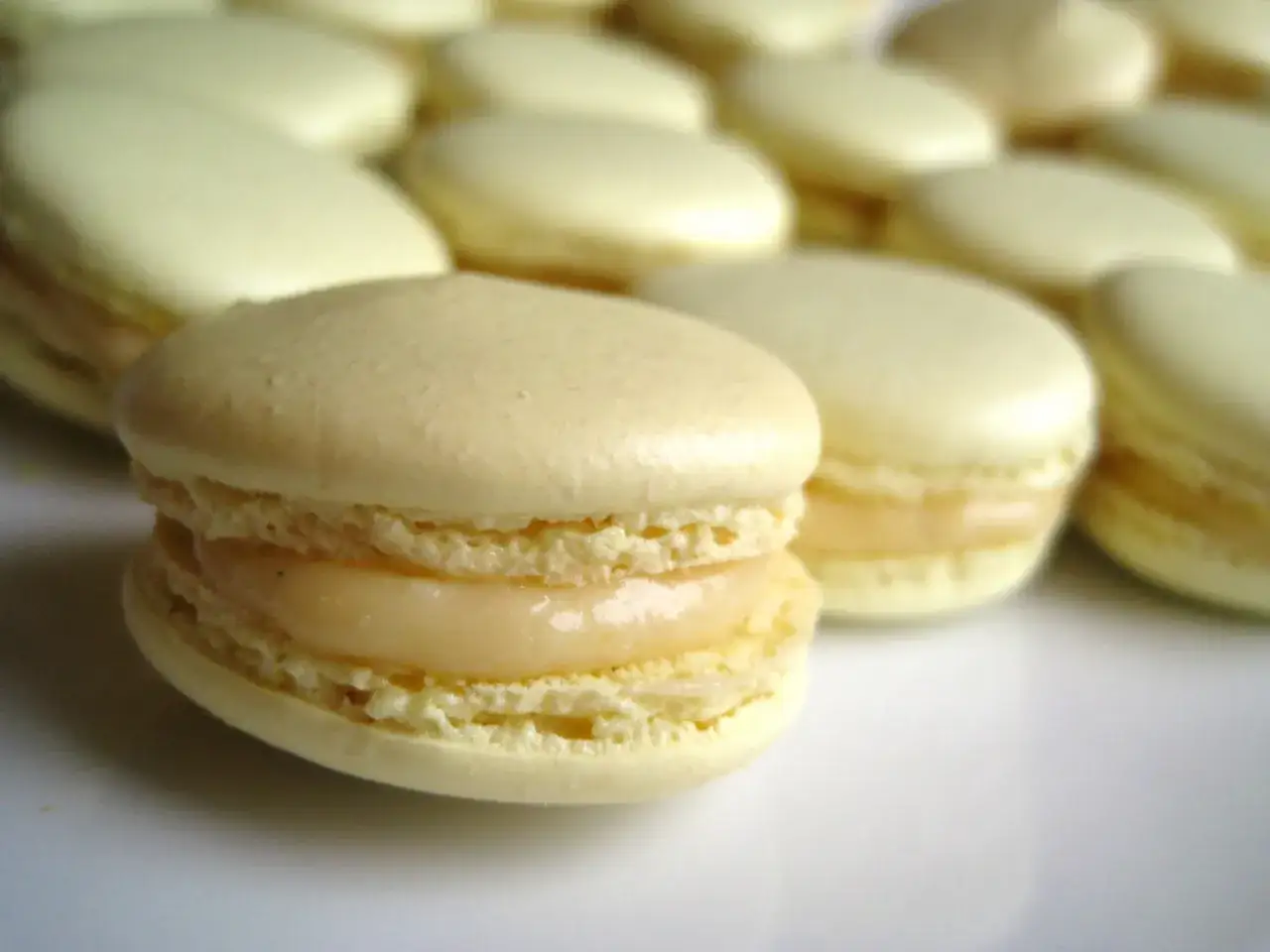 Un délicieux macaron meringue française, à la garniture crémeuse, se tient au premier plan, entouré d'autres macarons pâles.