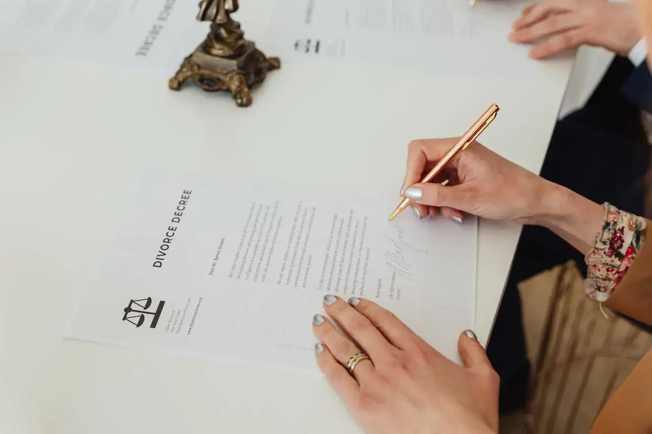Kobieta podpisuje dokument "DIVORCE DECREE". Wniosek o rozwód można pobrać online.