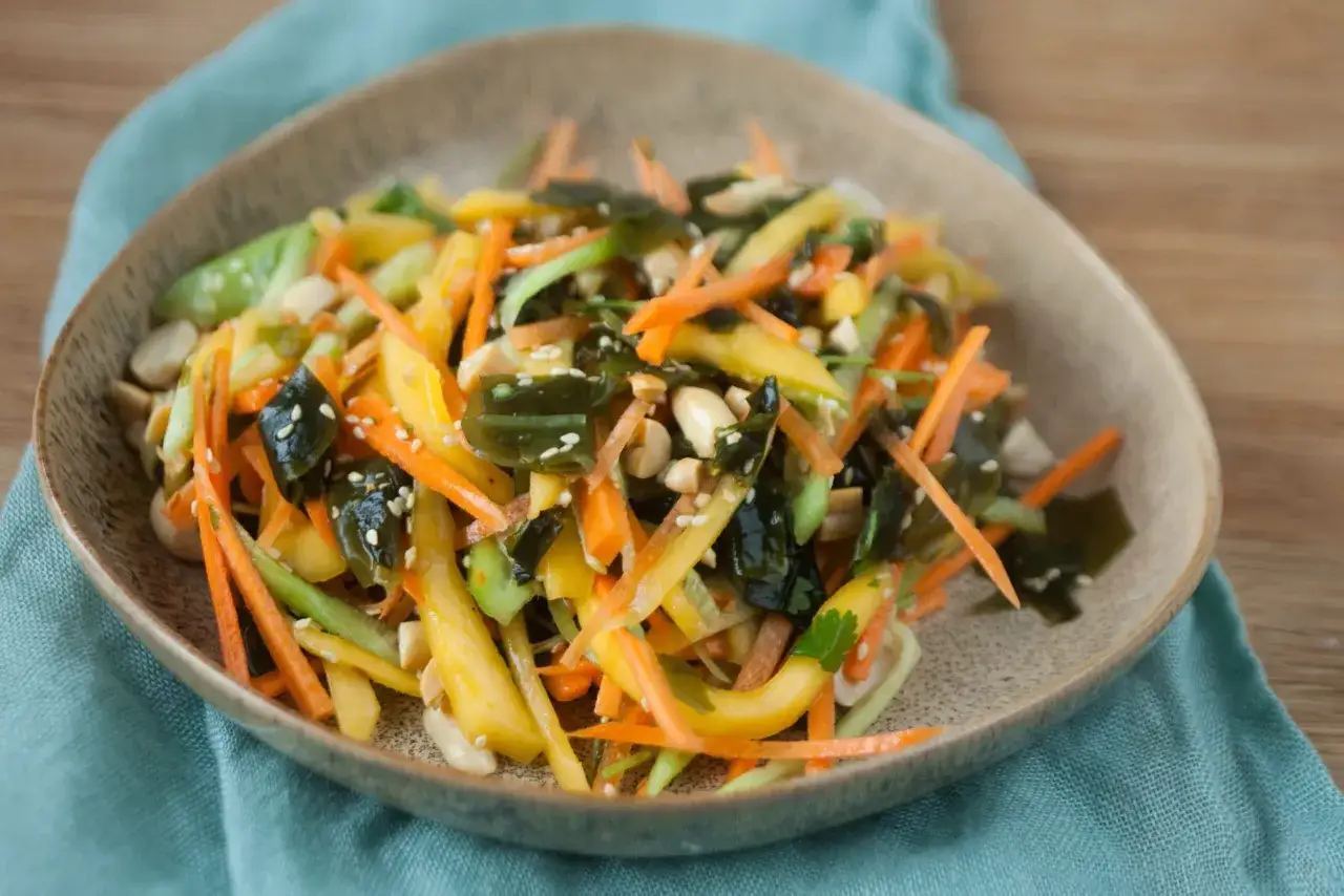 Kolorowa sałatka z mango, marchewką, ogórkiem i wodorostami, posypana sezamem i orzeszkami.