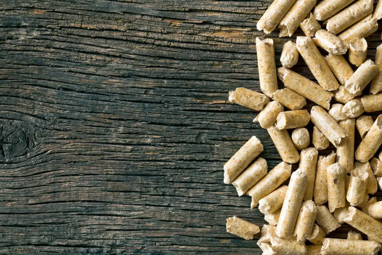 Drewniane deski i stos pelletu. Czy pellet jest ekologiczny? To pytanie zadaje sobie wielu, a ten obrazek pokazuje jego naturalne pochodzenie.