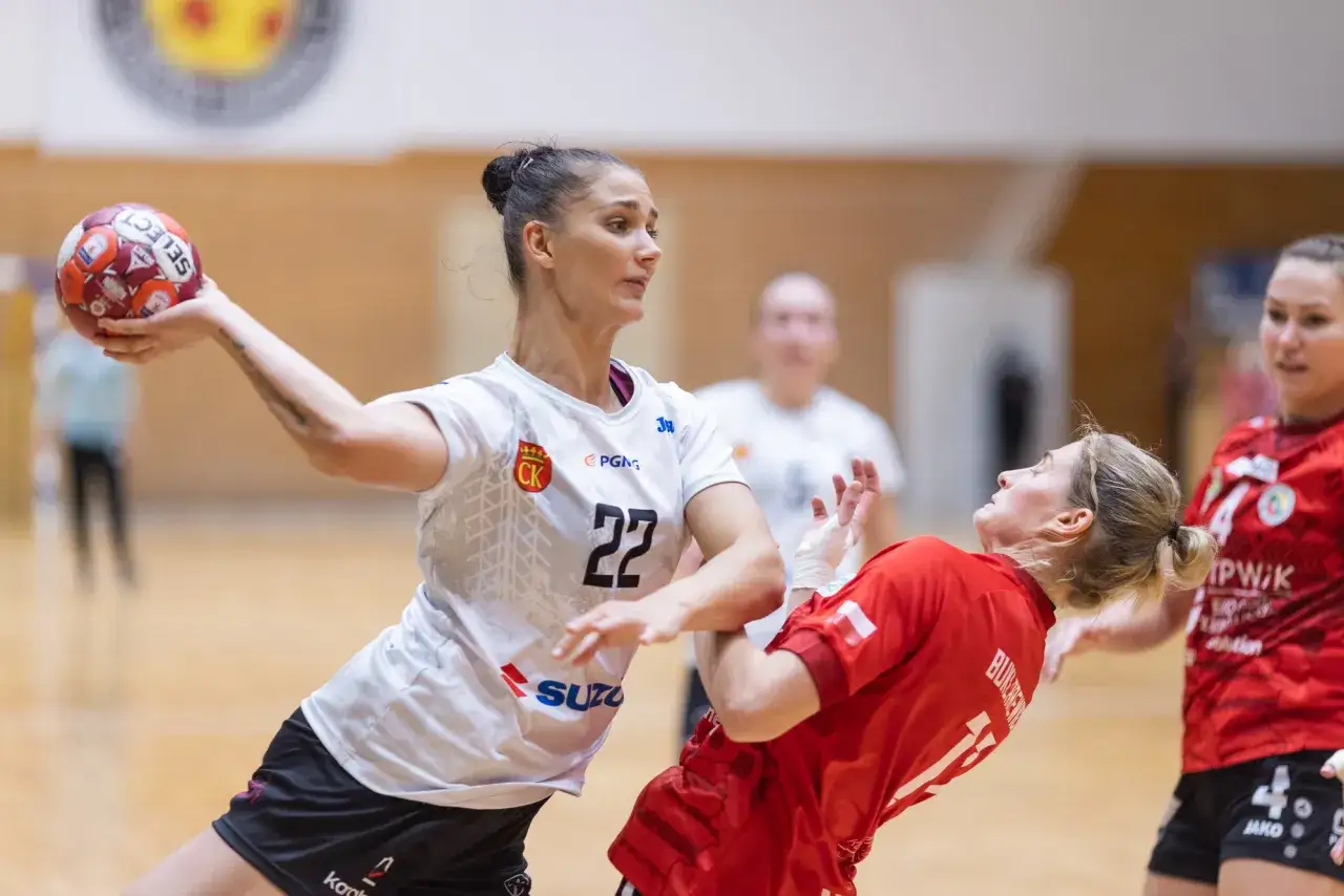 Piłkarka Suzuki Korona Handball Kielce rzuca piłkę. Rywalka w czerwonej koszulce próbuje ją zablokować.