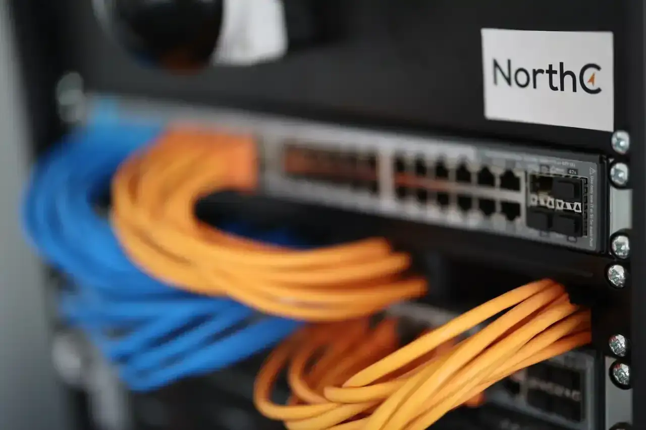 Netzwerkschrank mit blauen und orangen Kabeln, die an einen Switch angeschlossen sind.