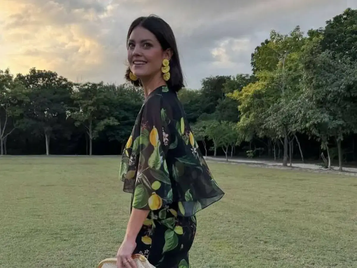 Isabelle Junot sonríe con un vestido estampado de limones, luciendo pendientes amarillos y un sombrero de paja en un día soleado.
