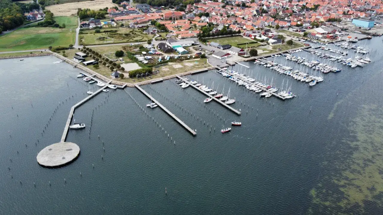 Luftaufnahme des Marstal Hafens mit vielen Segelbooten, die an Stegen liegen. Ein ovaler Steg mit Bänken ragt ins Wasser.