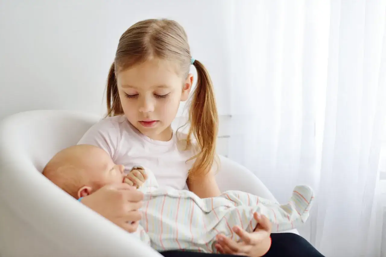 Starsza siostra delikatnie trzyma noworodka, ucząc się jak przygotować dziecko na rodzeństwo.