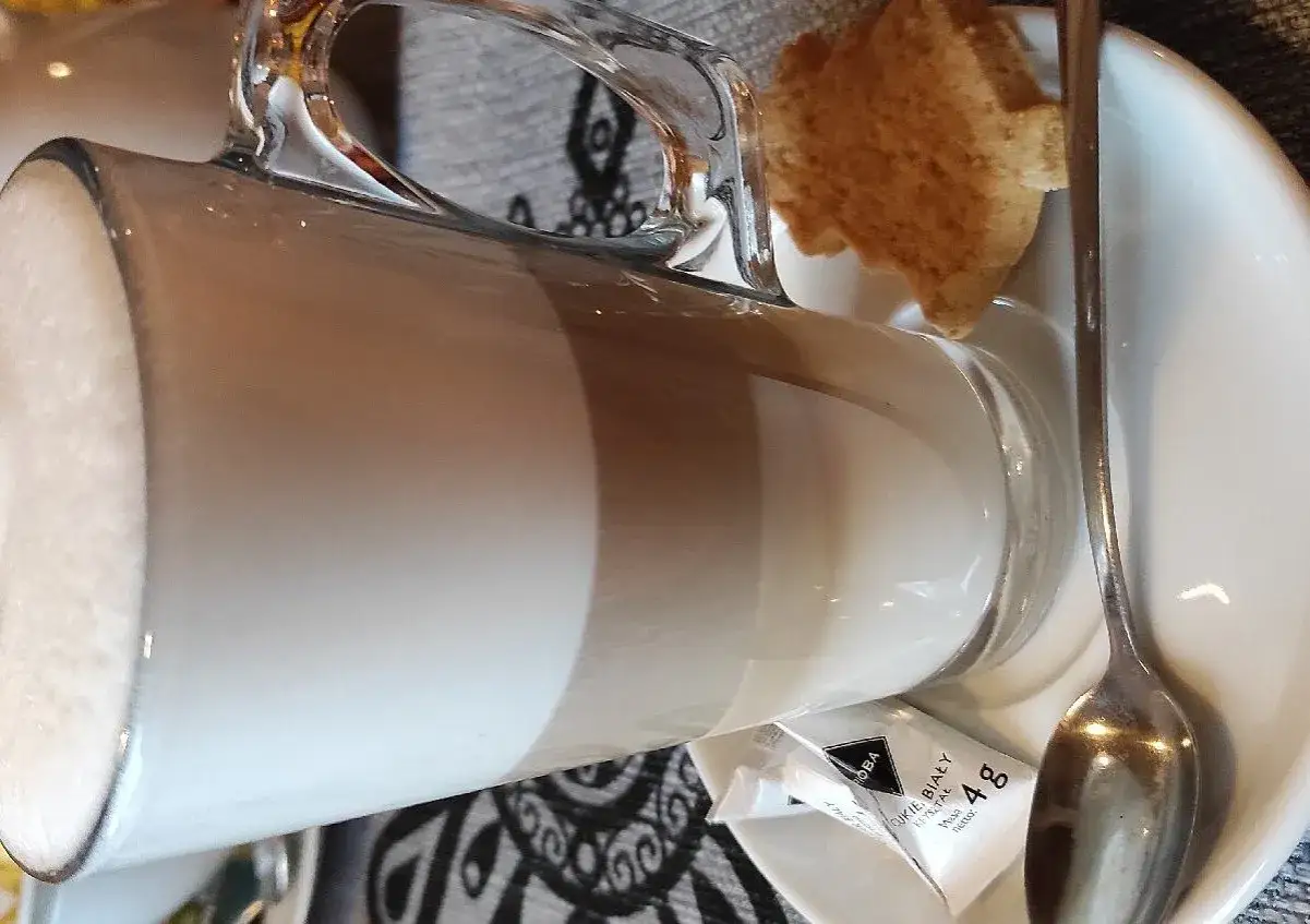 Kawa latte w szklance, obok ciasteczko i cukier. Idealna na przerwę w karczmie u wróbla menu.