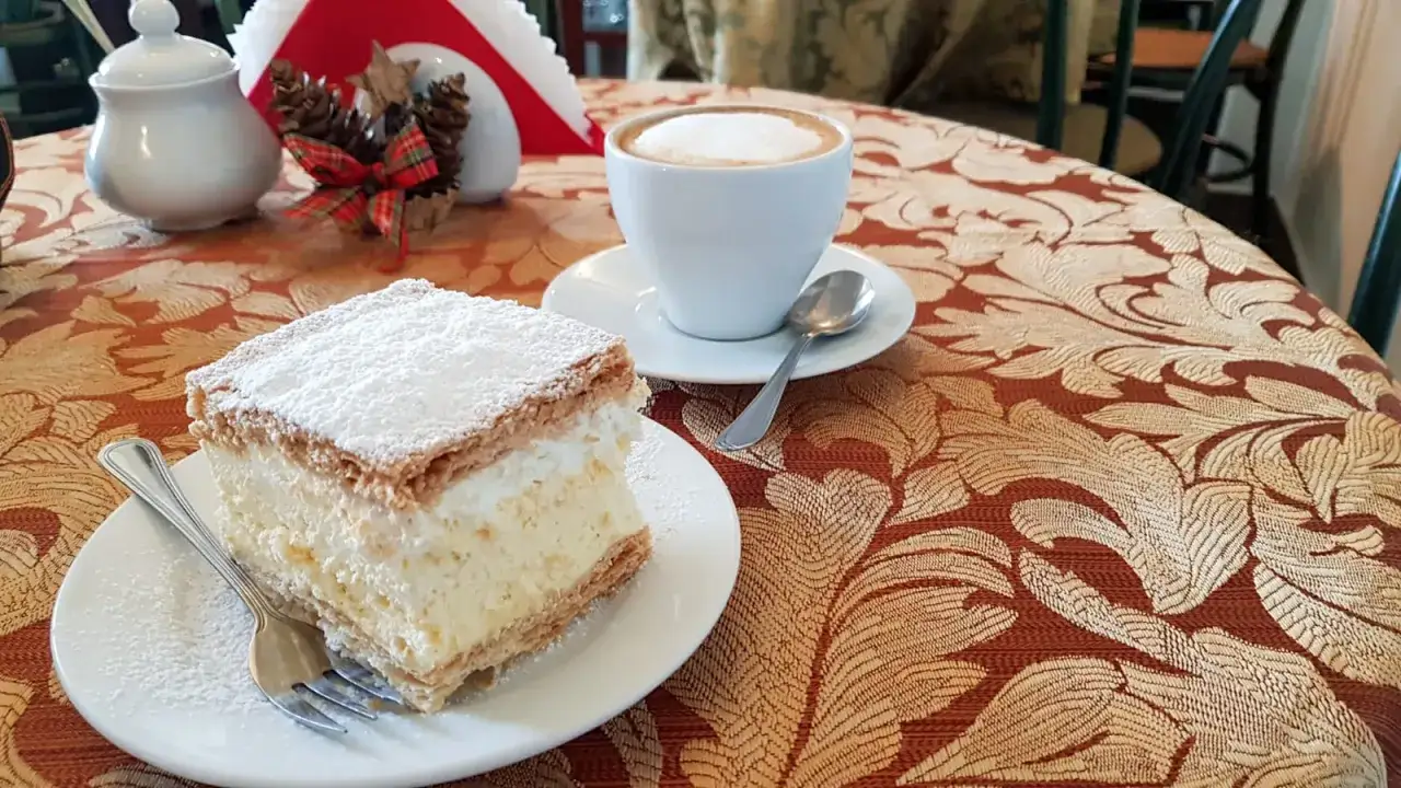 Kremówka posypana cukrem pudrem i filiżanka kawy na stoliku.